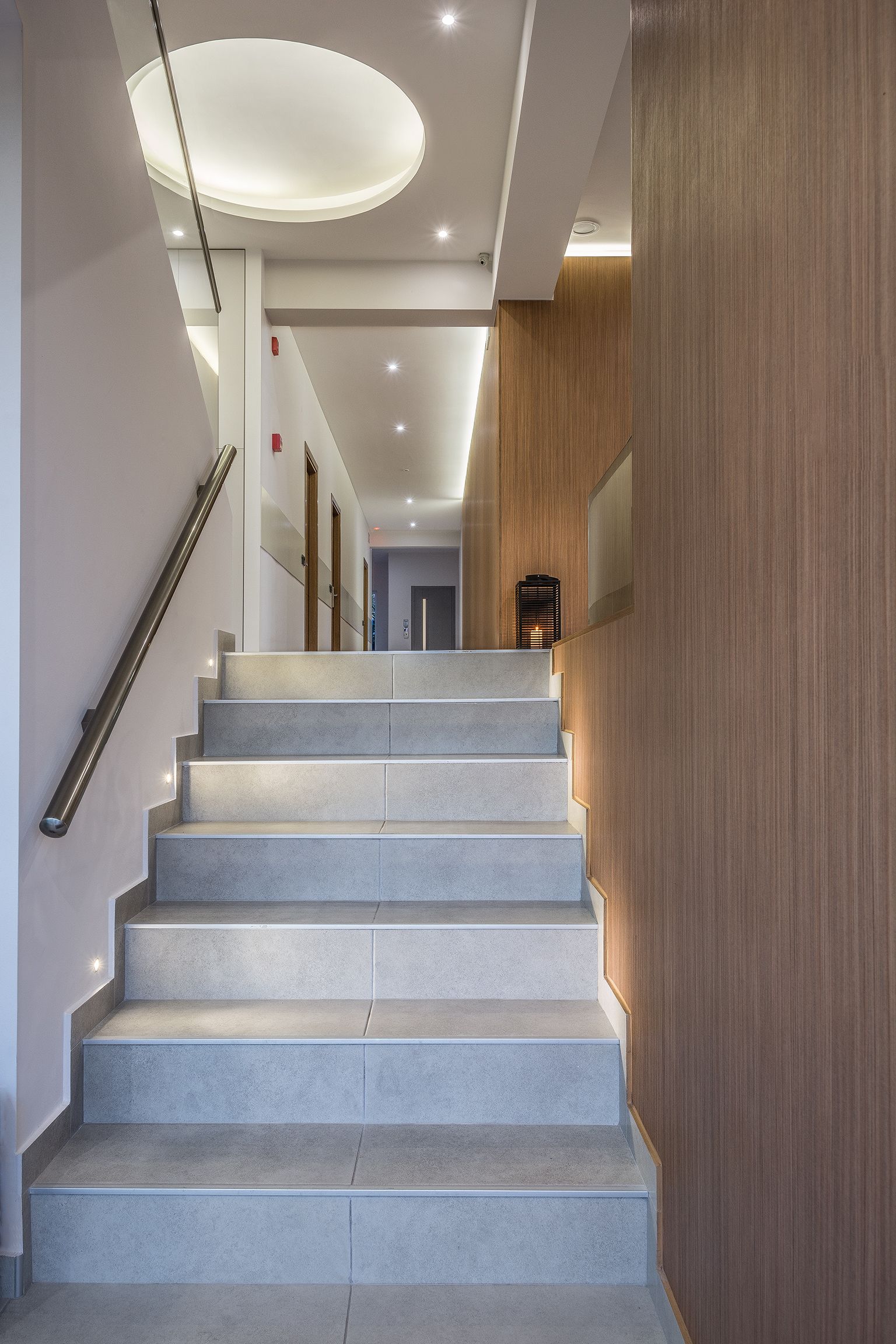 Una scala moderna con corrimano, che conduce a una piattaforma illuminata da un lampadario.