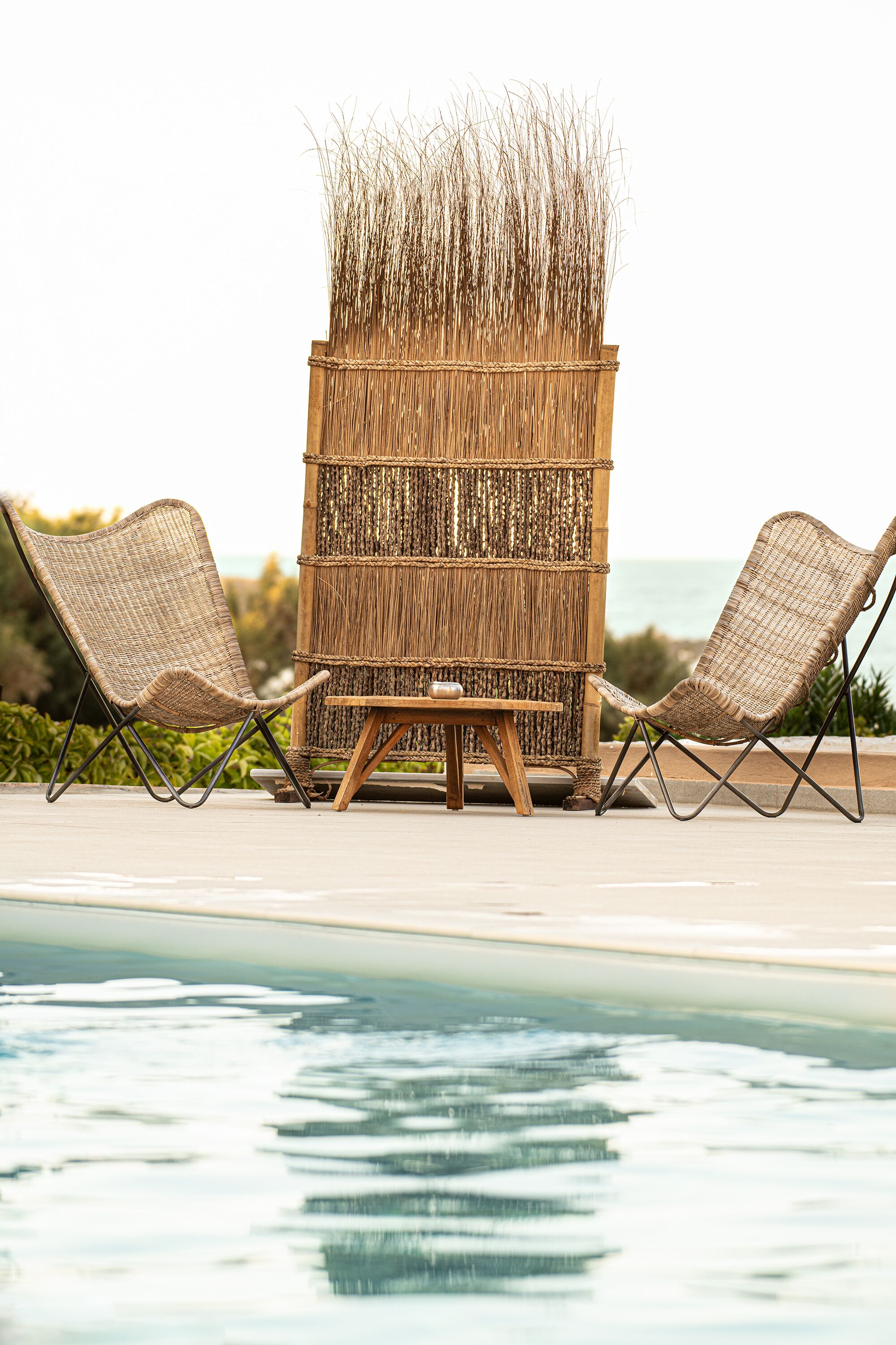 A poolside area with two wicker lounge chairs and a small wooden table.