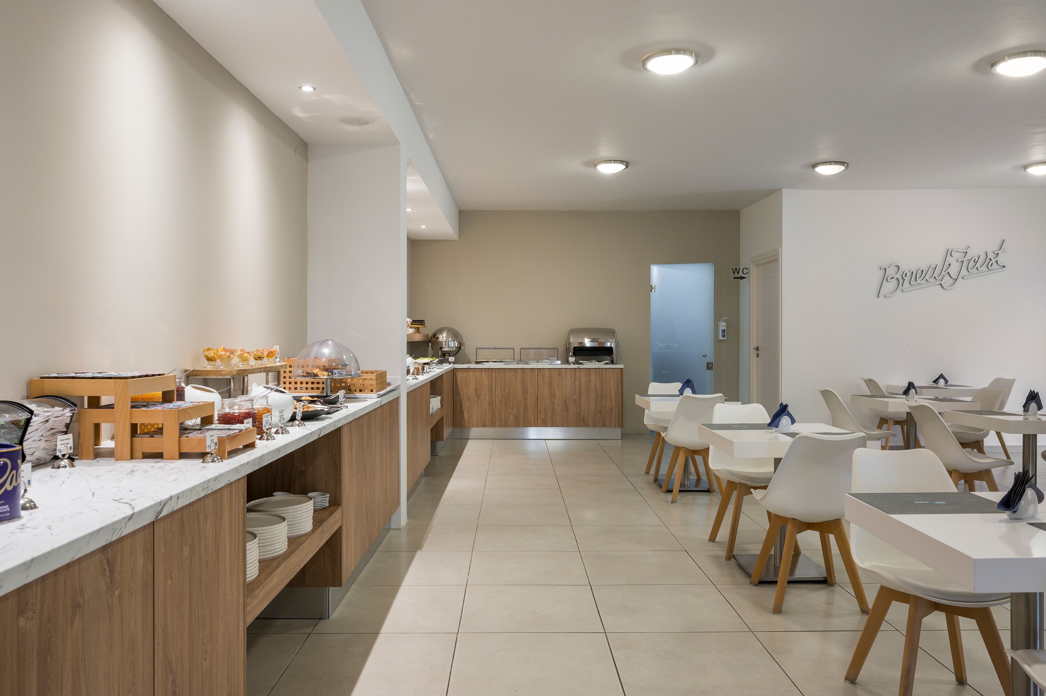 A modern breakfast area with a marble counter, wooden cabinets, and white chairs.