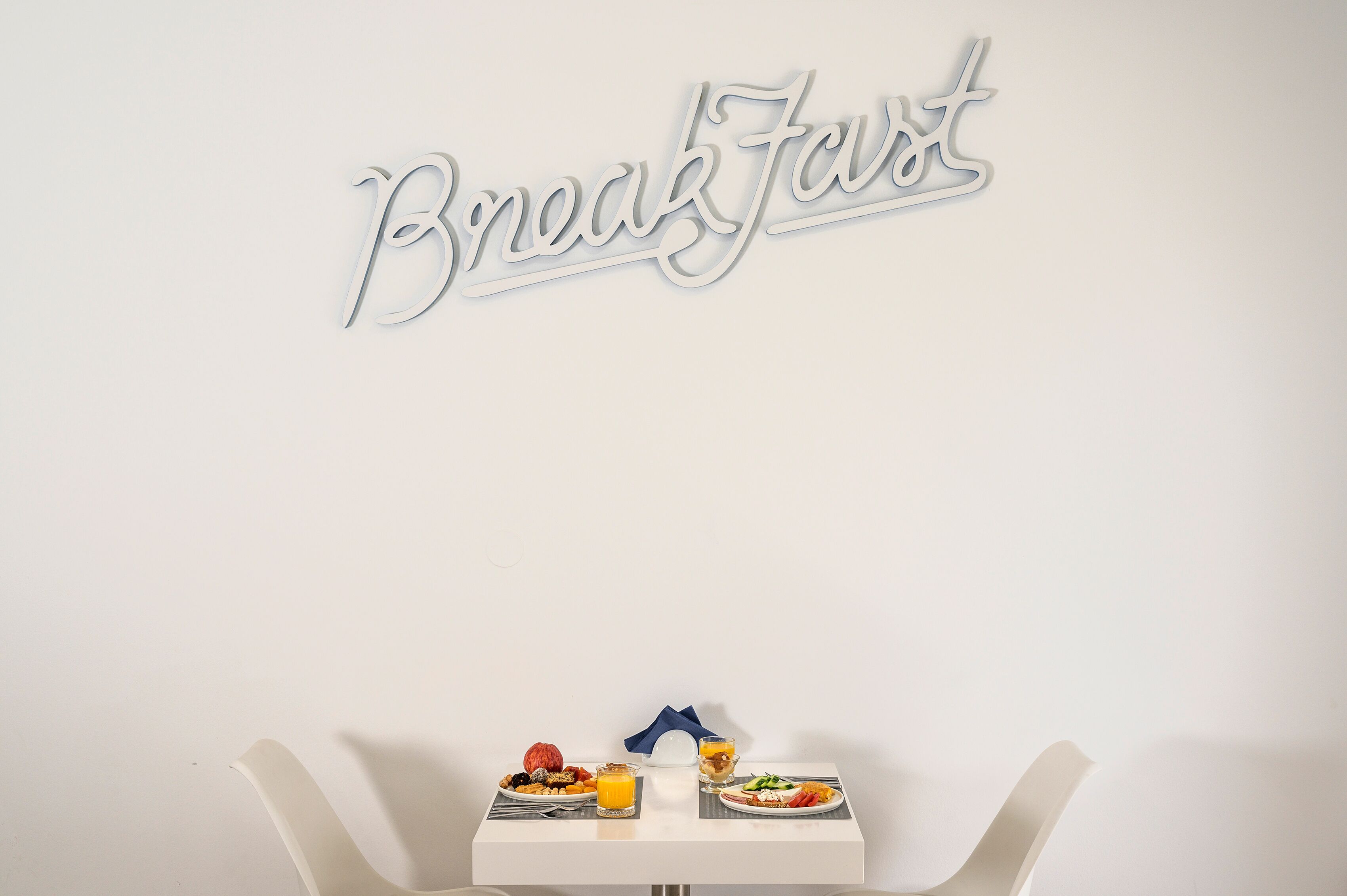 Una mesa con platos de comida y dos sillas blancas, junto a un letrero en la pared que dice "Breakfast".