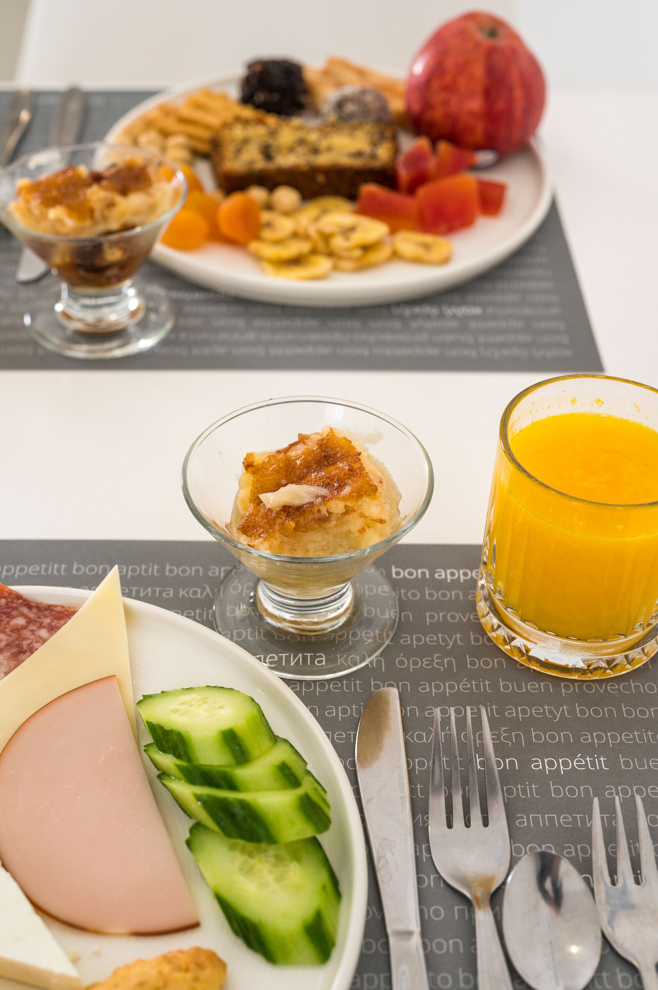 Un desayuno con un plato de comida, un vaso de zumo de naranja y un pequeño postre en un bol de cristal.