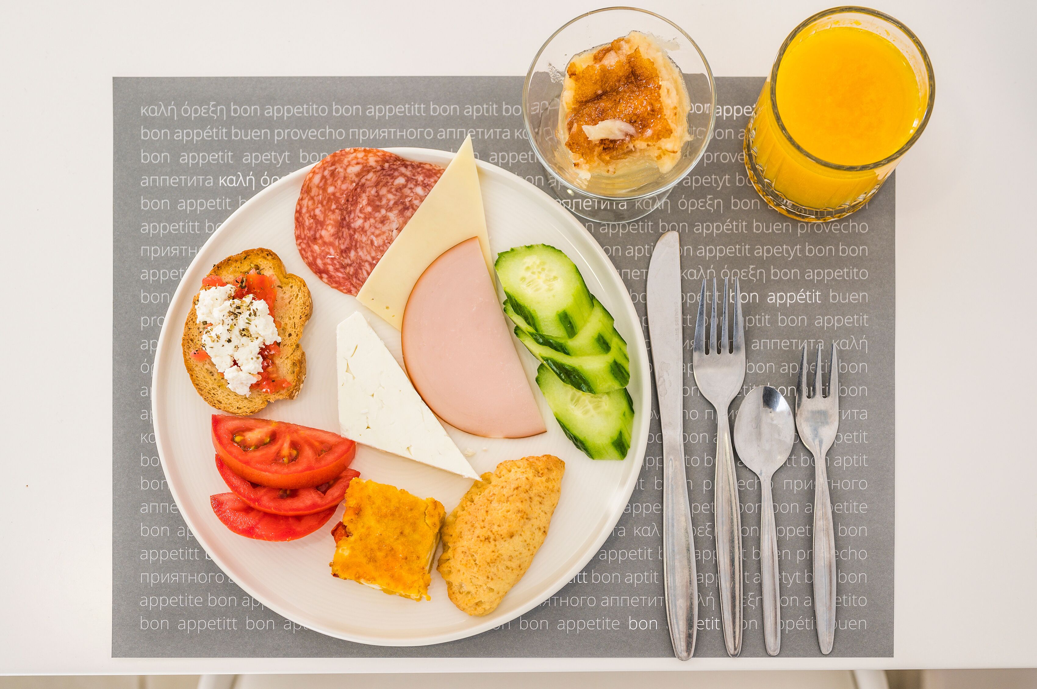 Une assiette contenant divers aliments, un verre de jus d’orange et des couverts sur une table dont le fond est imprimé.