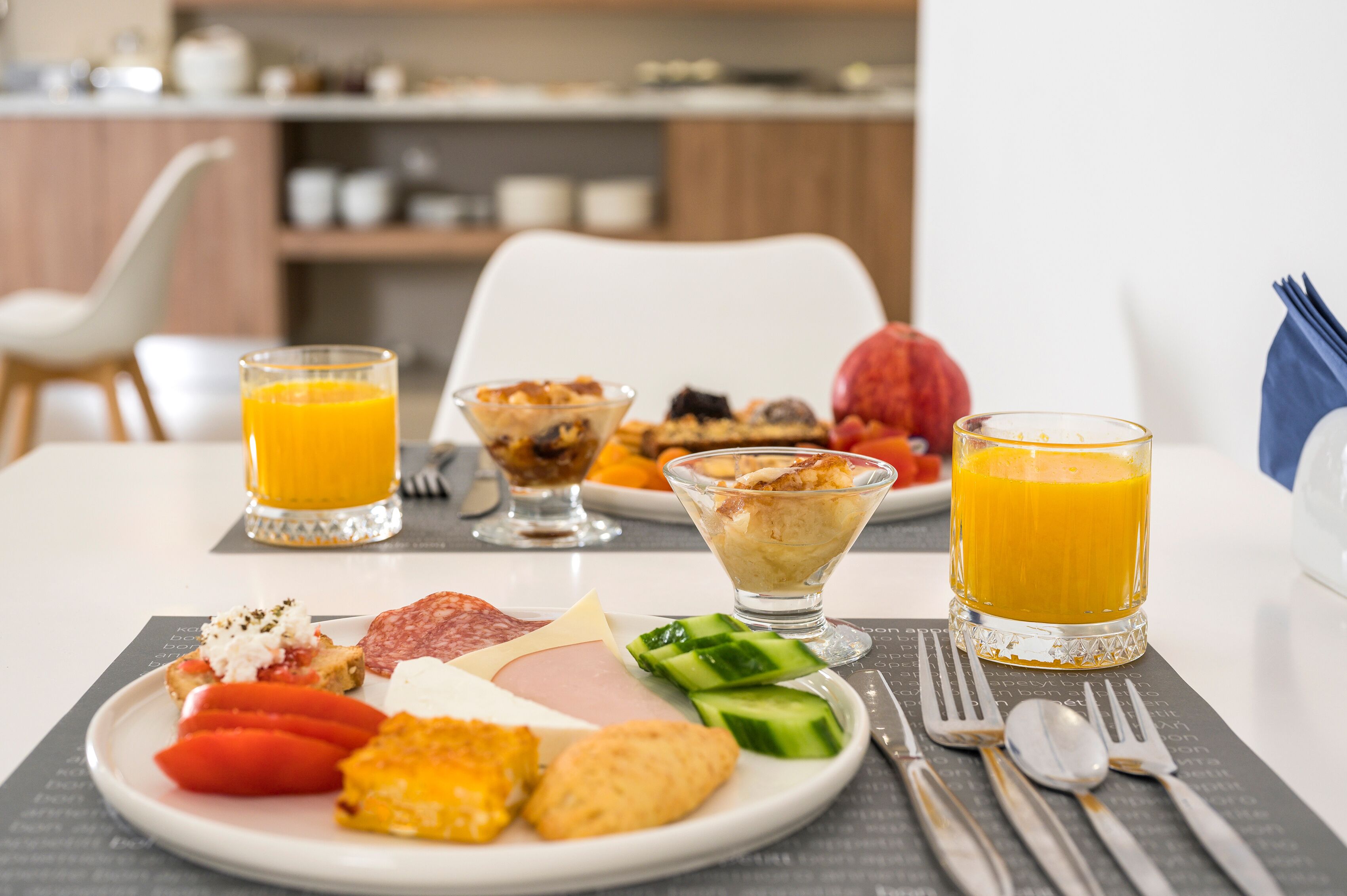Ein Frühstückstisch mit einer Platte mit verschiedenen Speisen, zwei Gläsern Orangensaft und einer Schüssel Müsli.
