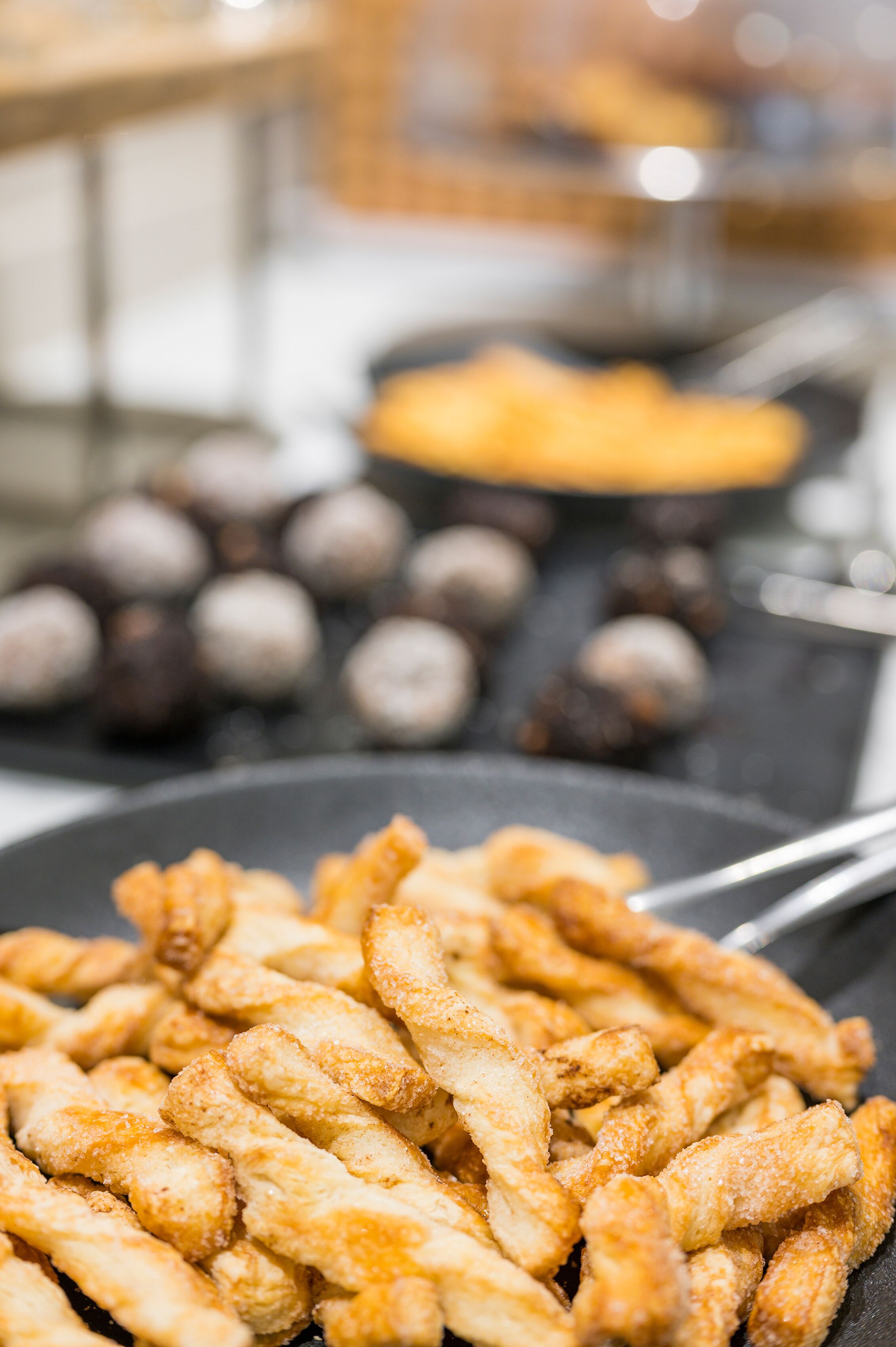 A close-up of fried dough sticks with a blurred background of other food items.