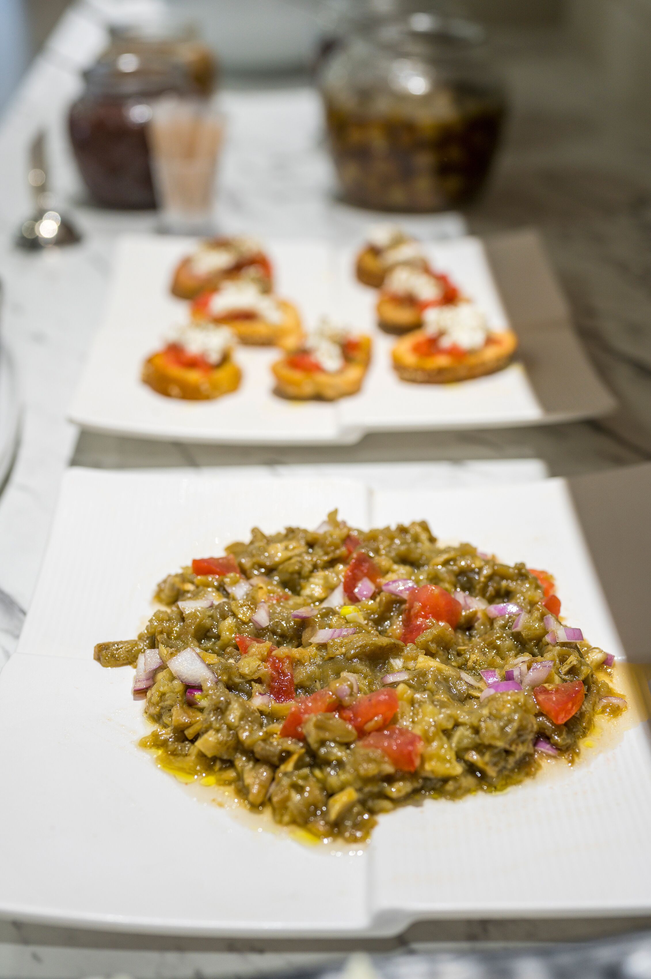 A table with two plates of food, one with a green vegetable dish and the other with small appetizers.