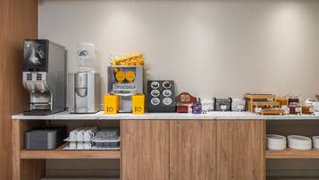 A modern breakfast bar with a coffee machine, water dispenser, and various food items.