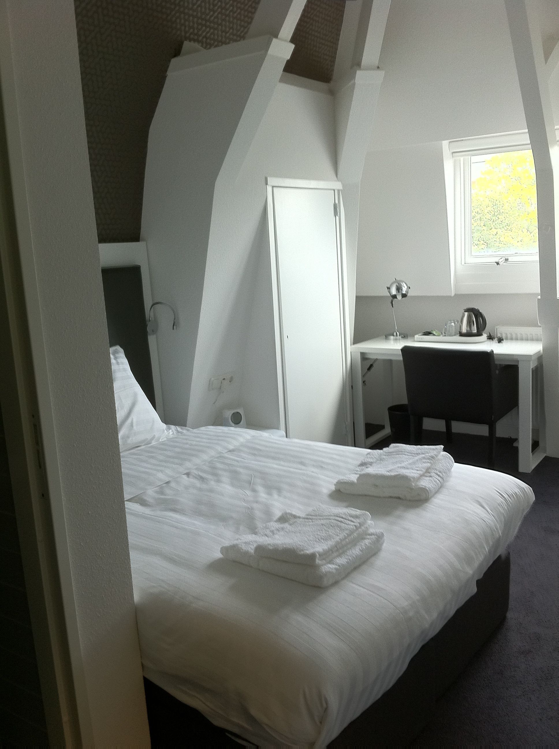A bedroom with a bed, a desk, and a window.