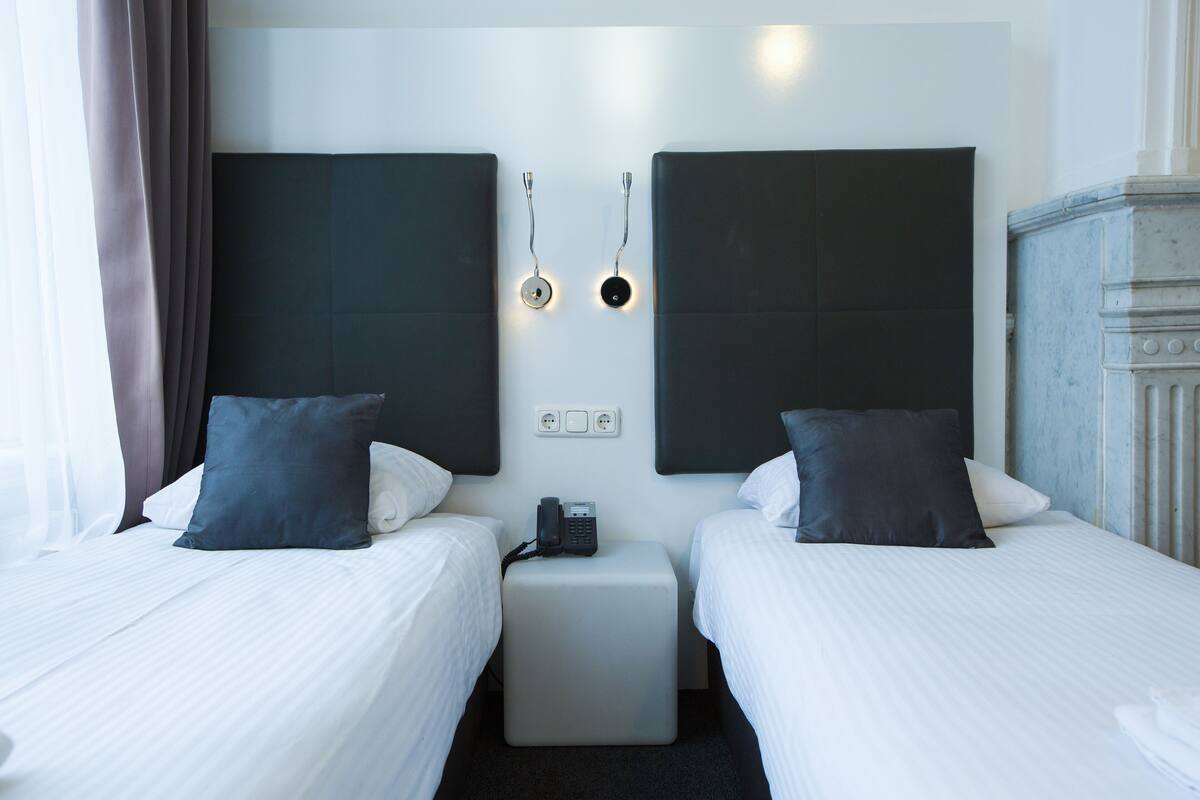 Ett hotellrum med två sängar, ett litet bord, en telefon och en väggmonterad lampa.