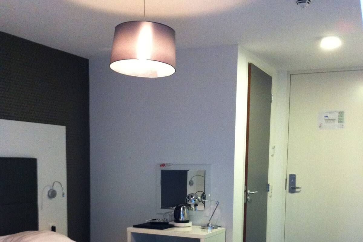 Ett hotellrum med en säng, sängbord, ett skrivbord, en stol, en spegel och en dörr.