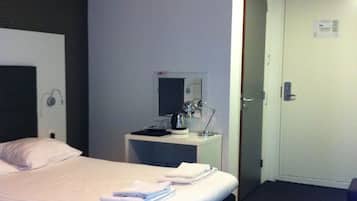 Habitación de hotel con cama, mesitas de noche, escritorio, silla, espejo y puerta.