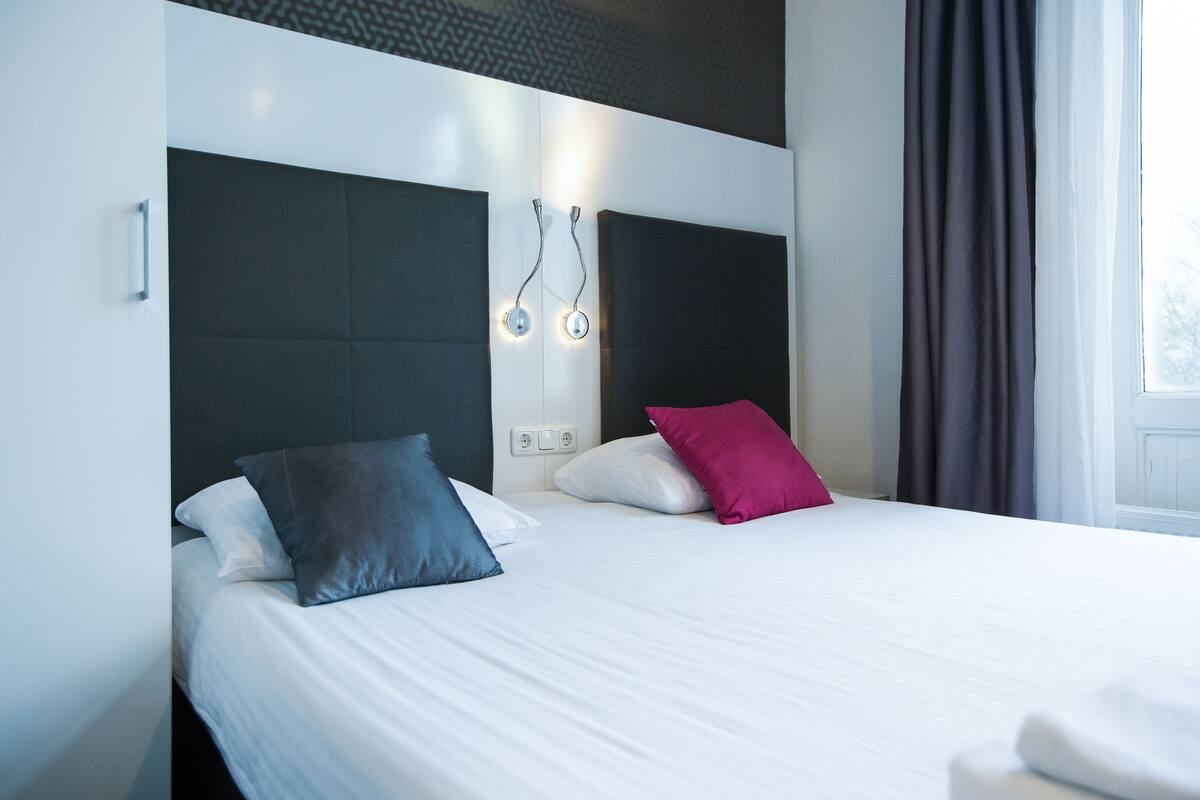 Ett hotellrum med en stor säng, två kuddar, en sänggavel och ett fönster med gardiner.