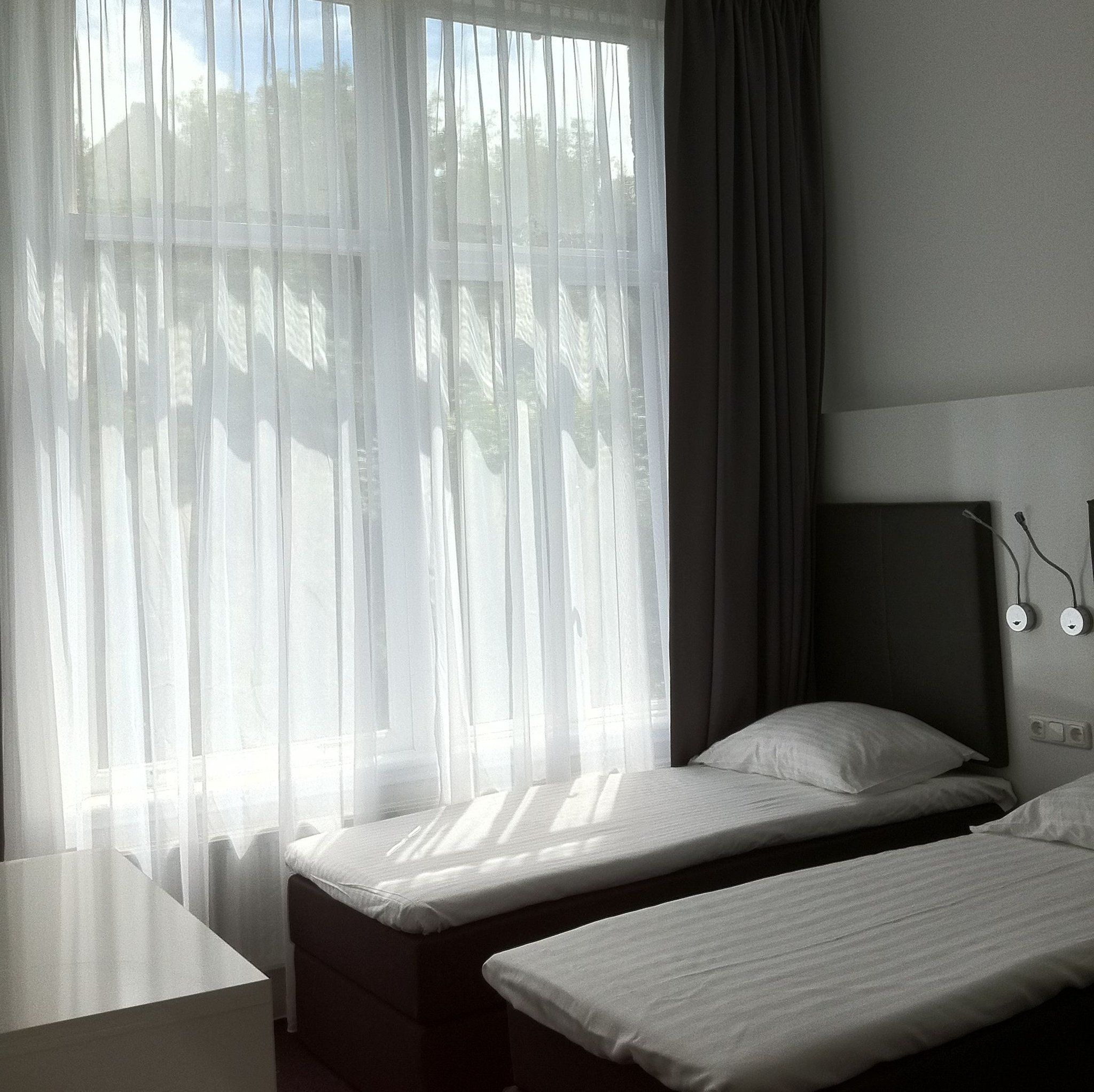 A hotel room with two single beds, a desk, and a window with sheer curtains.
