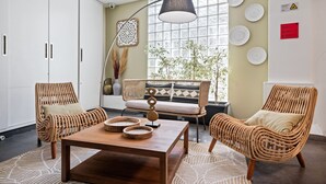 Un salon moderne avec des meubles en osier, une table basse en bois et une grande fenêtre ornée d’assiettes décoratives.
