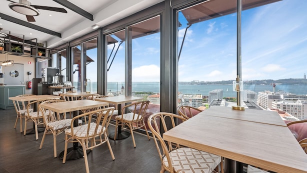 Un espace repas moderne avec de grandes fenêtres, des meubles en osier et une vue sur la ville et la mer.
