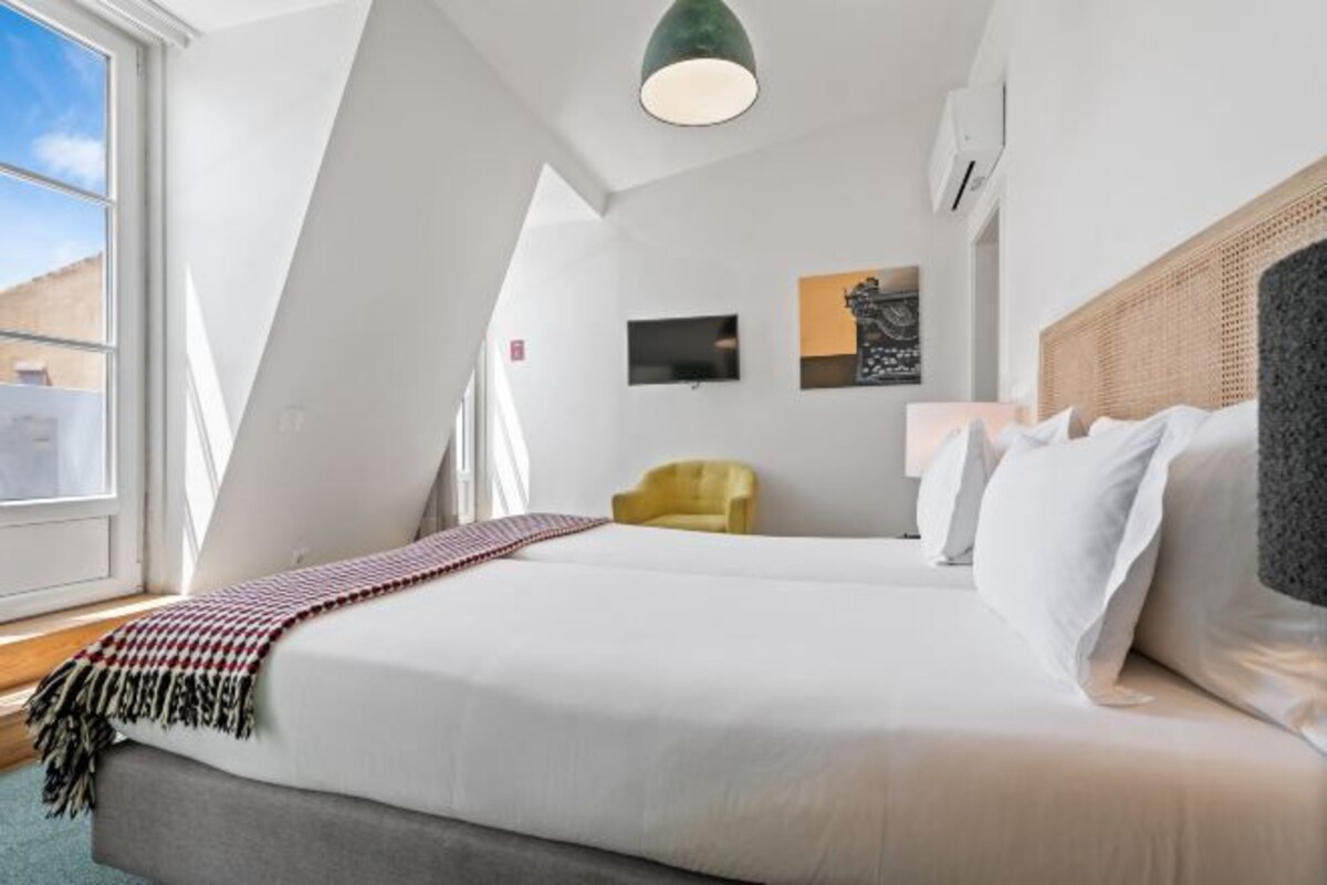 A modern hotel room with a large bed, a yellow armchair, and artwork on the walls.