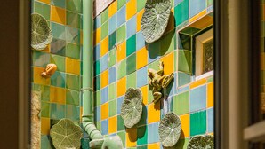 Une salle de bain avec des carreaux de mosaïque aux couleurs vives, un grand tuyau vert et divers éléments décoratifs, comme des grenouilles et des feuilles.