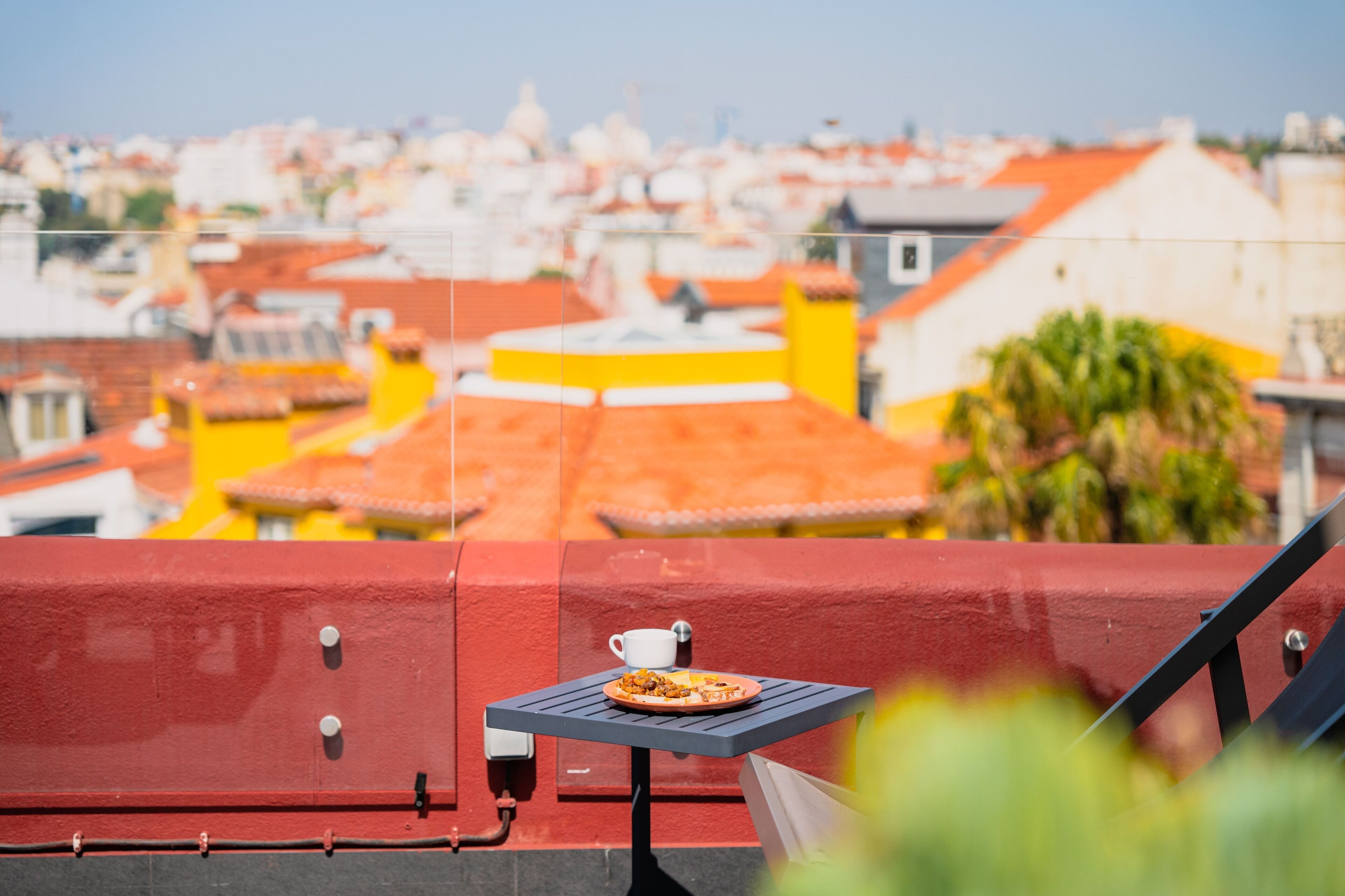 A red railing with a small table and a cup, overlooking a cityscape with colorful buildings.