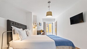 Une chambre d’hôtel moderne avec un grand lit, une table de chevet, une lampe, un téléviseur fixé au mur et une fenêtre avec des rideaux.