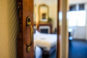 A wooden door with a brass handle leading to a room with a bed and a dresser. - Hôtel du Chêne (Itxassou)