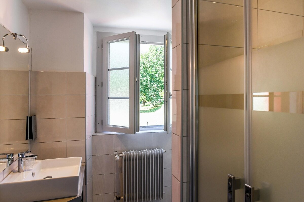 A modern bathroom with a large sink, a mirror, a window, and a radiator.