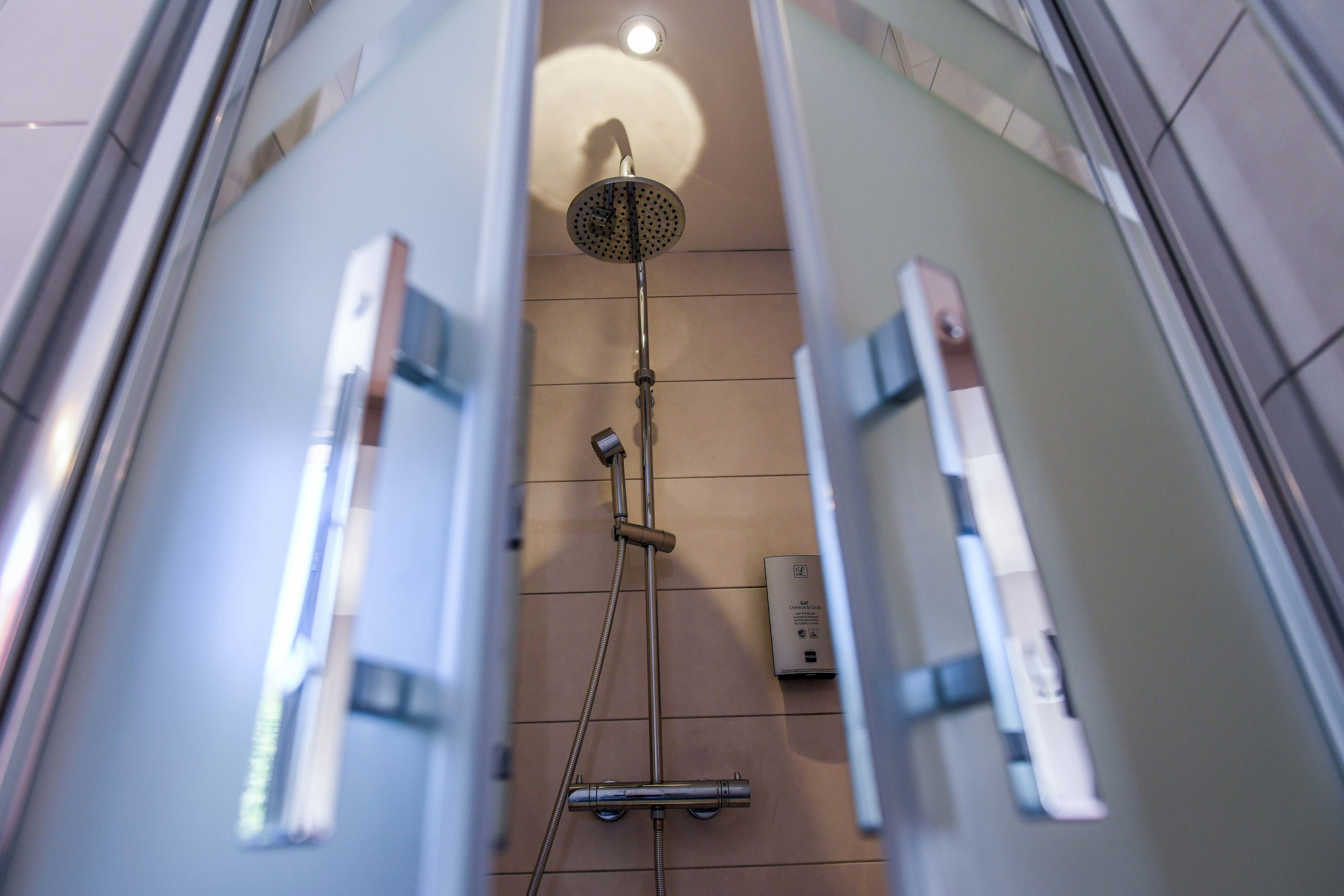 A glass-enclosed shower with a handheld showerhead and a wall-mounted control panel.