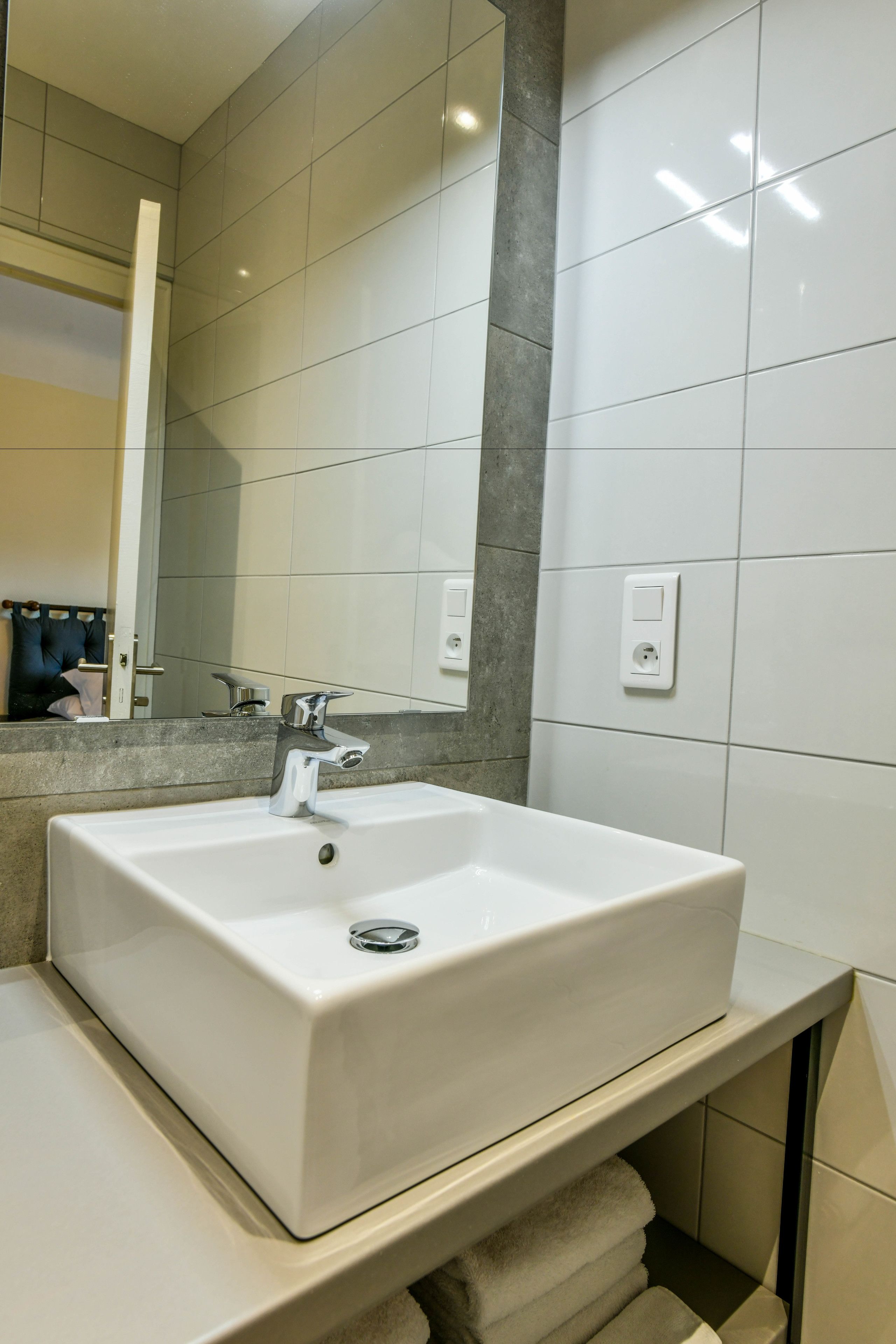 A modern bathroom with a large white sink, a mirror, and a towel rack.