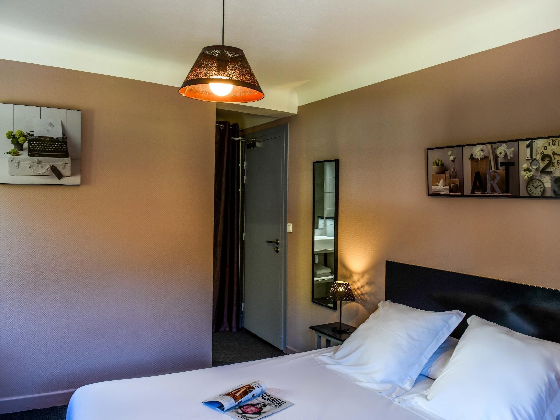 A hotel room with a bed, a hanging lamp, a mirror, and a wall art piece.