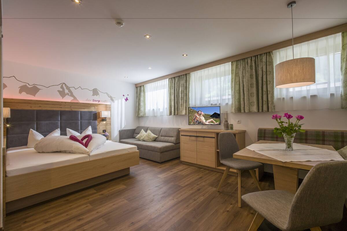 A modern, well-lit room with a bed, sofa, dining table, and a TV.