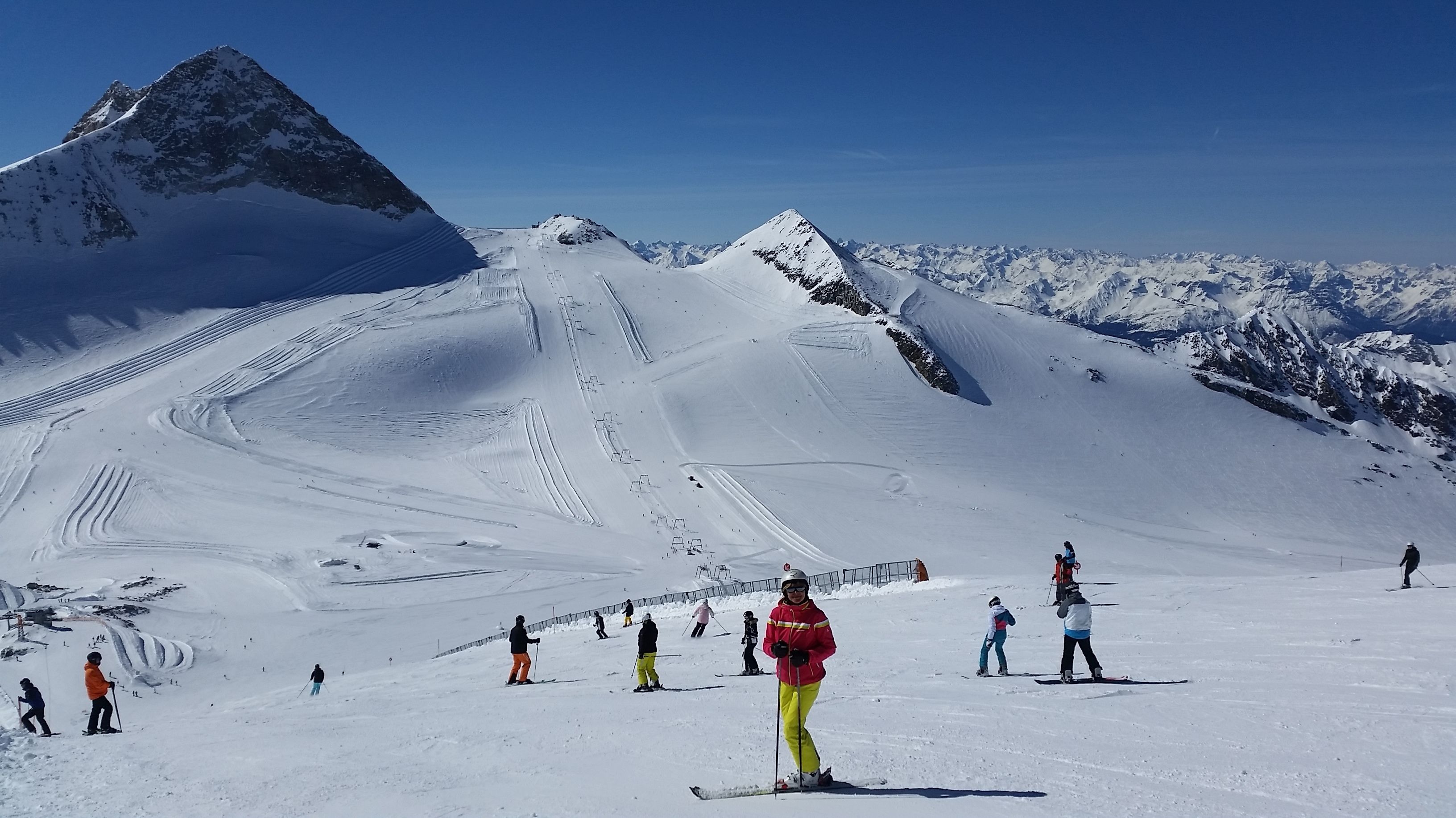 Een besneeuwde skipiste met skiërs en een berg op de achtergrond.