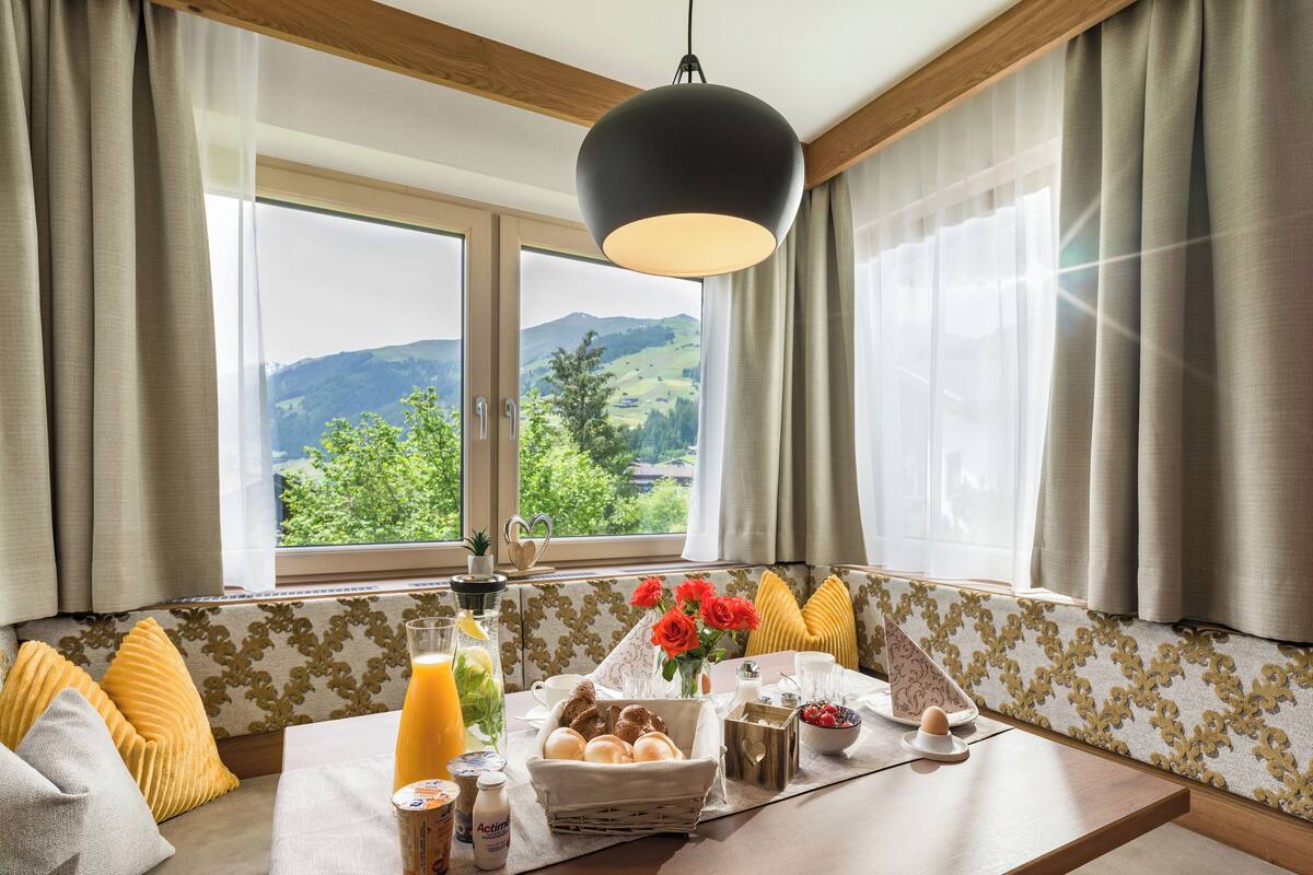A breakfast setup with a table, breakfast items, and a view of mountains through the window.
