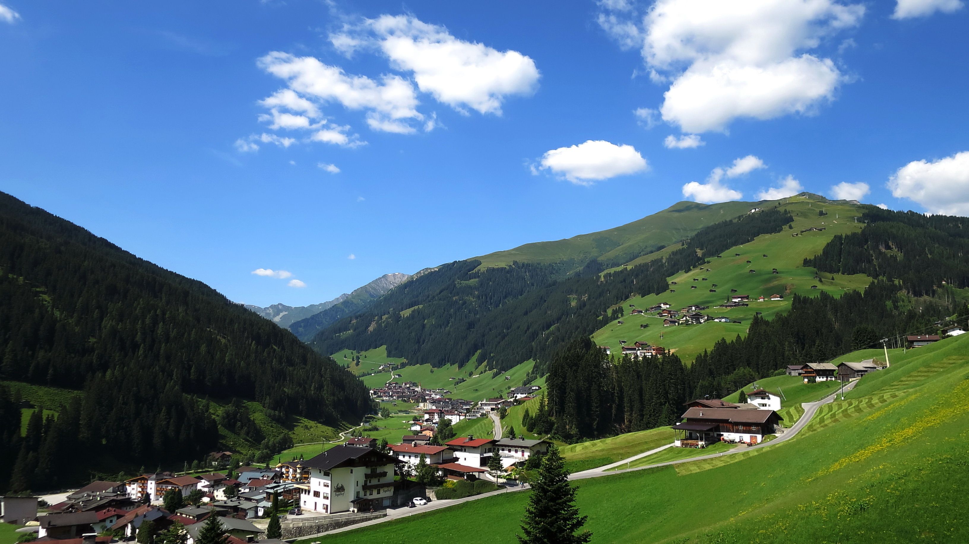 A mountain village with traditional houses, a winding road, and a valley.