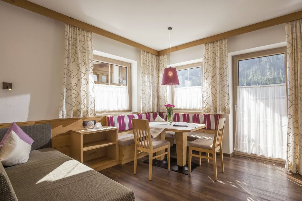A cozy room with a wooden dining table, chairs, a sofa, and a TV.