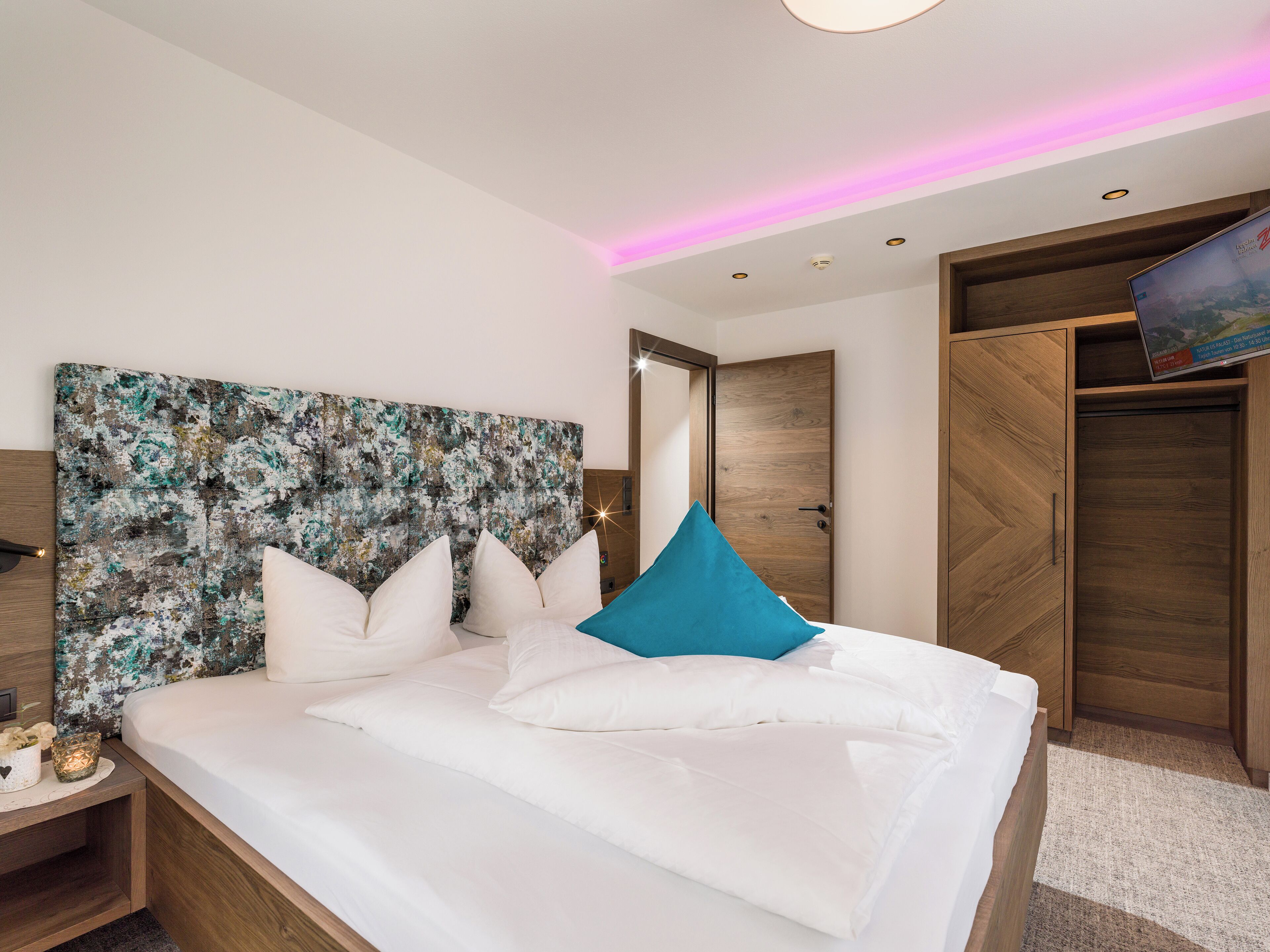 Quarto moderno com uma cama grande, cabeceira de madeira, televisão e guarda-roupa.