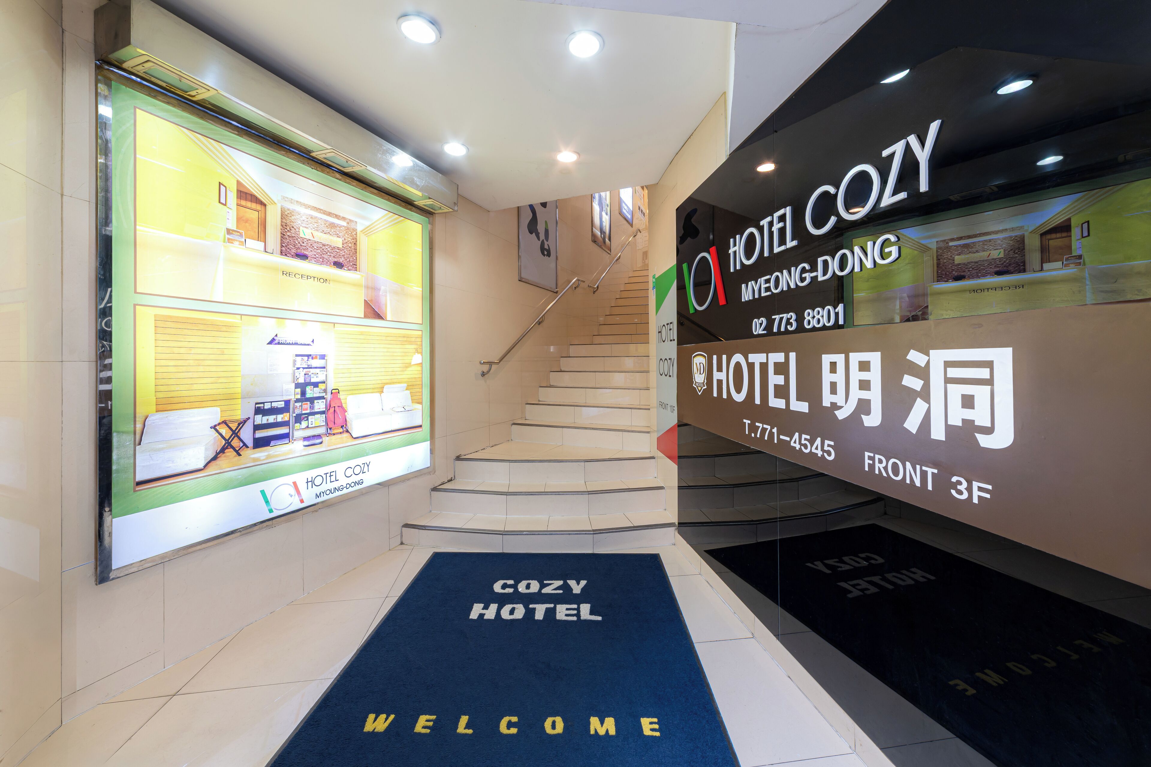 A hotel entrance with a reception desk, a staircase, and a welcome mat.