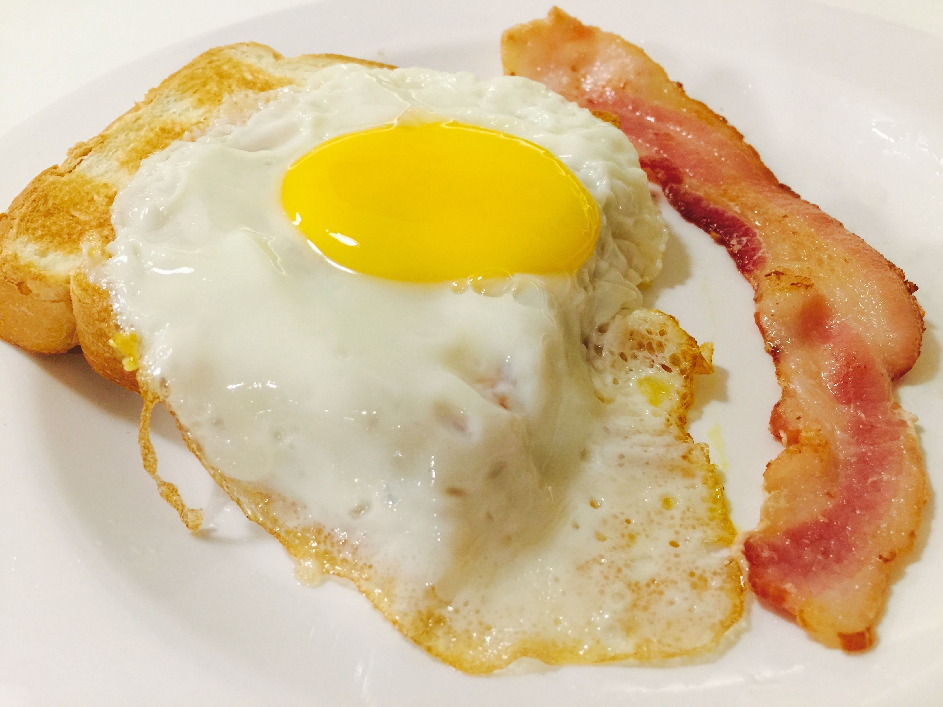Une assiette de petit-déjeuner avec un œuf au plat, des toasts et du bacon.
