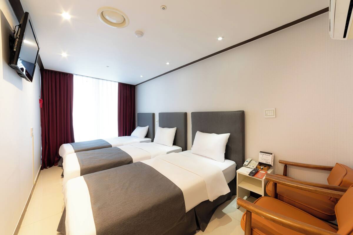 A hotel room with two beds, a TV, a desk with a phone, and a chair.