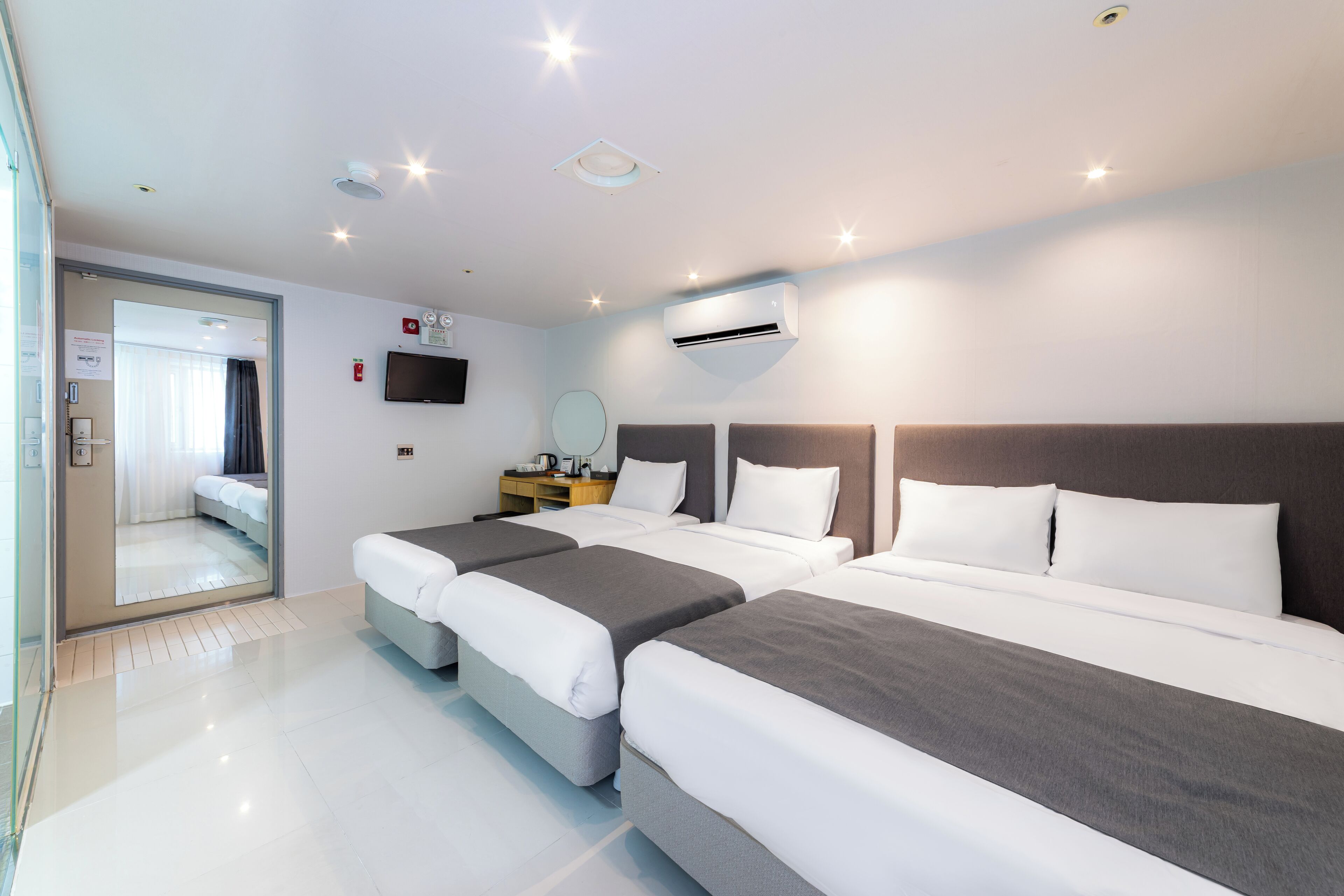 Ein Hotelzimmer mit drei Betten, einem Flachbildfernseher, einer Klimaanlage und einem Nachttisch mit Lampe.