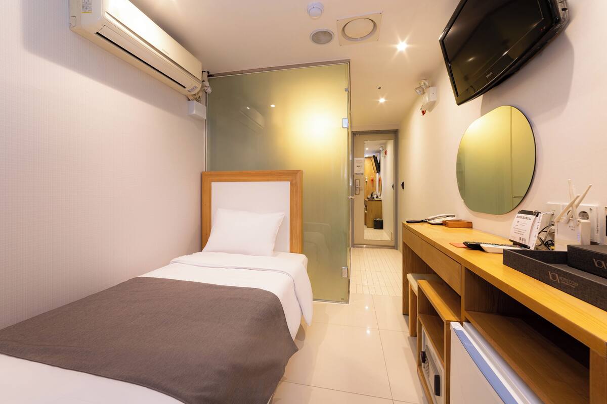 A hotel room with a bed, a desk, a mirror, and a TV.
