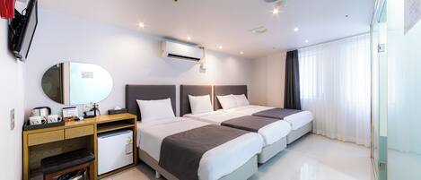 Habitación de hotel con dos camas, un escritorio con computadora, un refrigerador pequeño y un cesto de basura.