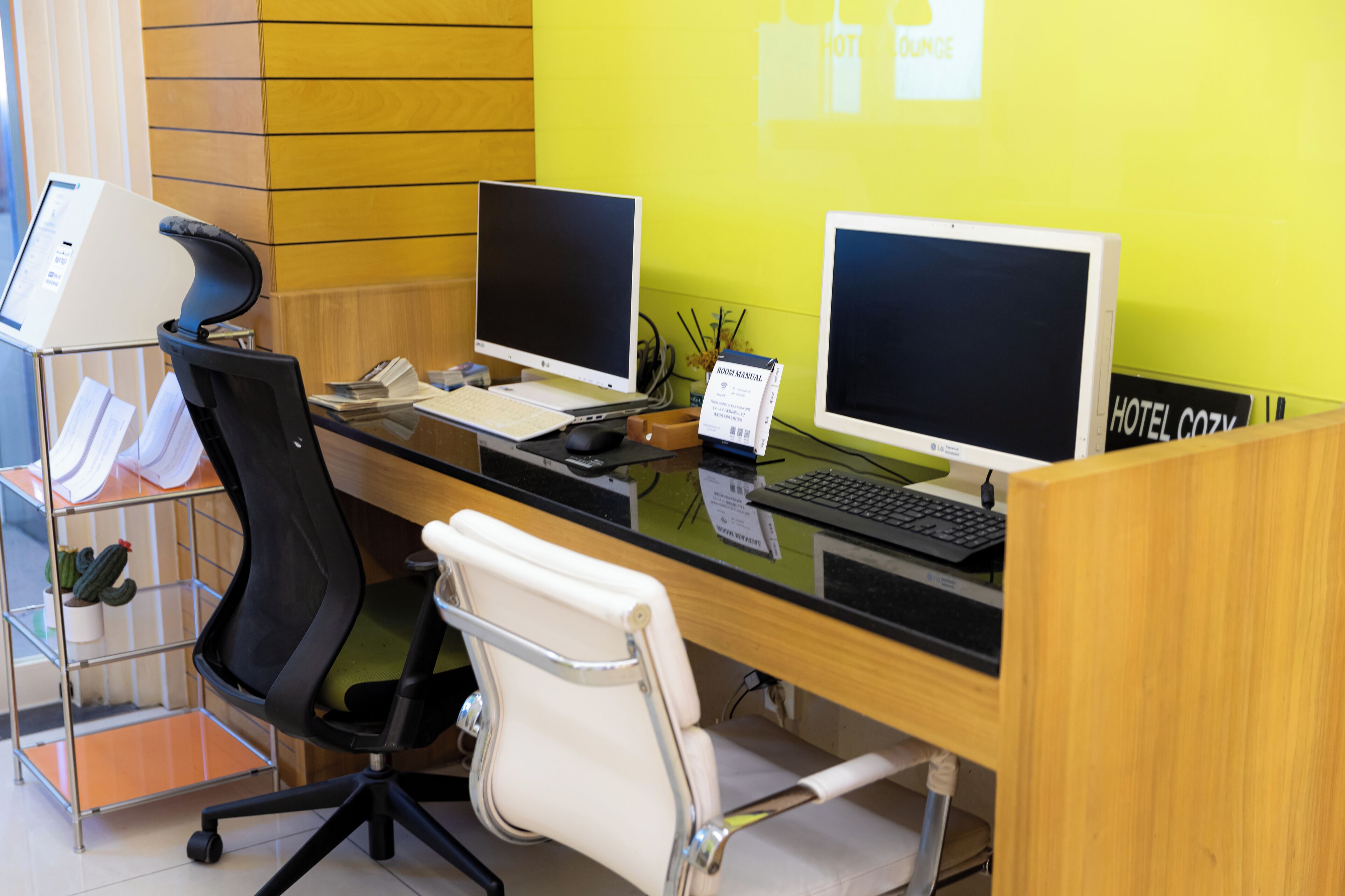 A hotel reception desk with two computer monitors, a telephone, and a laptop.