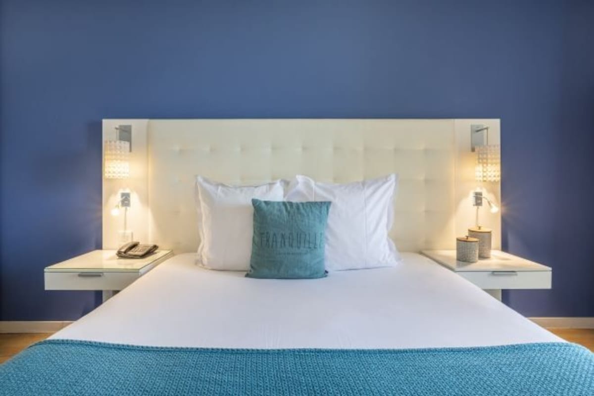 Un lit avec une literie blanche, un oreiller turquoise et deux lampes de chevet.