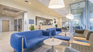 Een moderne lobby met blauwe en bruine zitplaatsen, een receptiebalie en een glazen wand met uitzicht.
