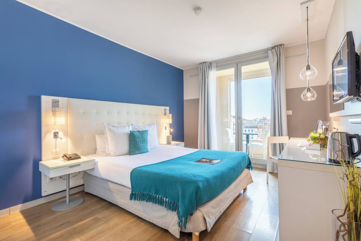Een moderne hotelkamer met een groot bed, een nachtkastje met een lamp, een flatscreen televisie en uitzicht op de stad.