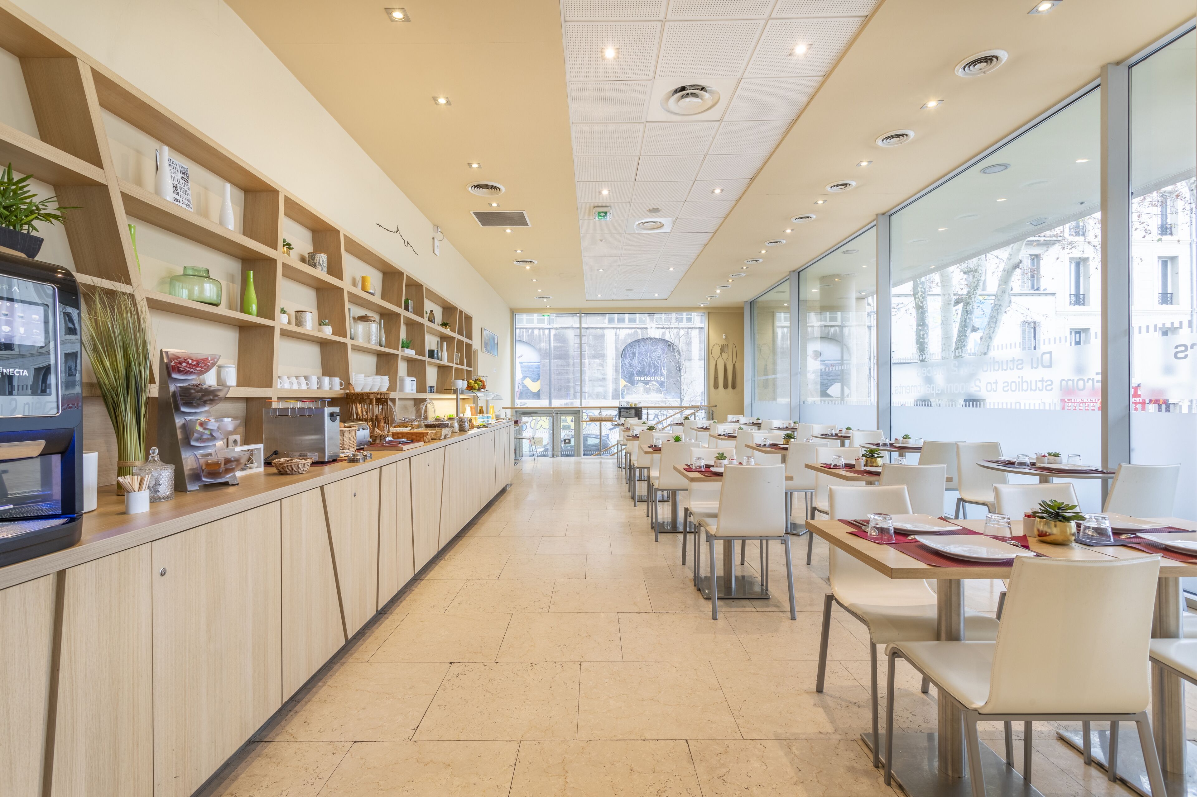 Un restaurant moderne avec un long comptoir, des étagères remplies d’ustensiles de cuisine et des tables avec des chaises.