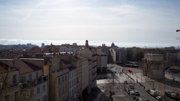 A cityscape with historic buildings, a central square, and a distant view of mountains.