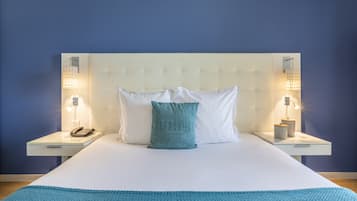 Un lit bien fait, avec une tête de lit blanche, deux tables de chevet avec des lampes, un coussin turquoise et un plaid bleu.