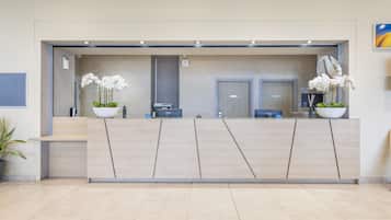 Un mostrador de recepción de diseño moderno, dos orquídeas blancas en macetas, un espejo y una puerta al fondo.
