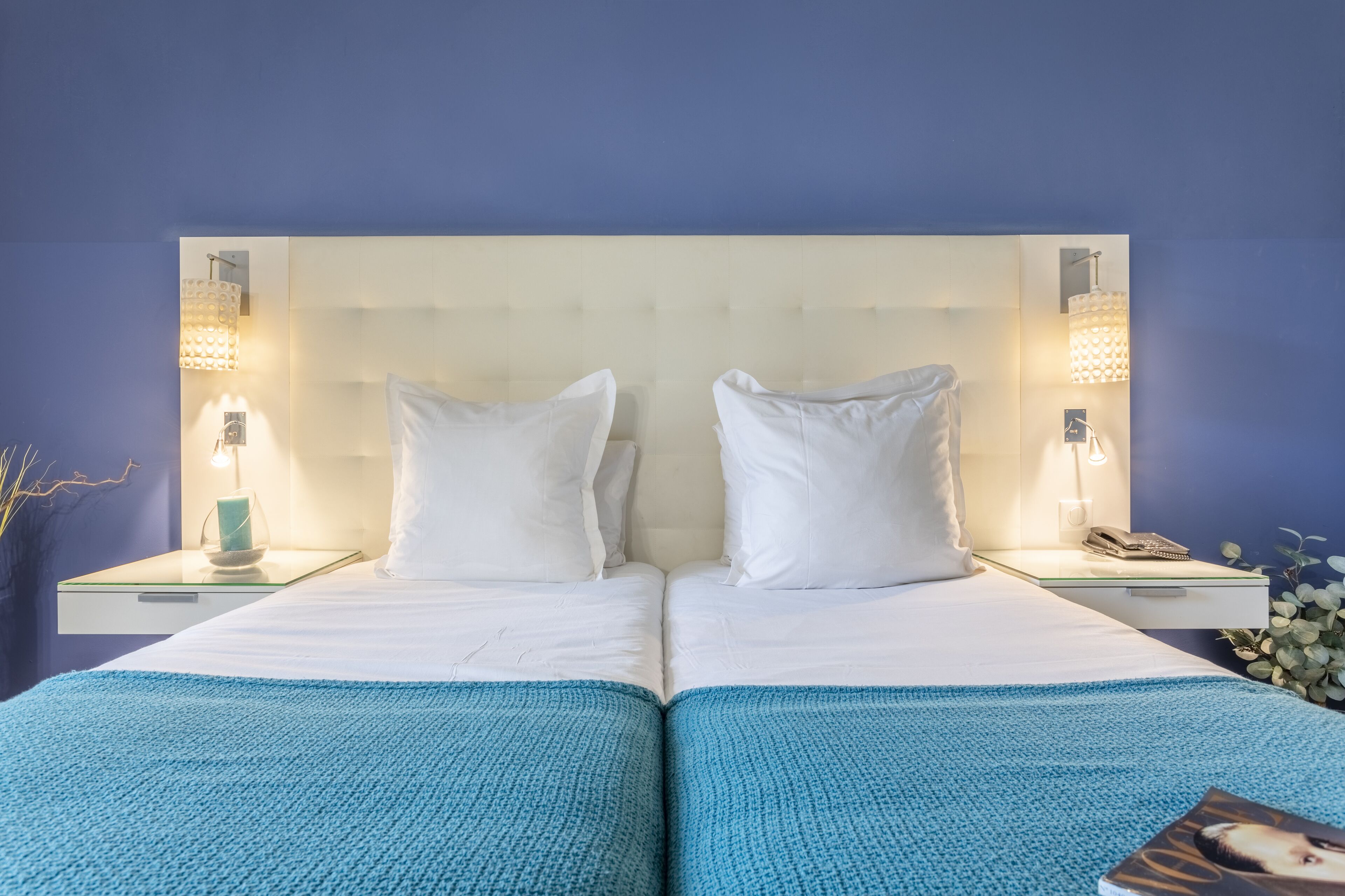 Een tweepersoonsbed met witte lakens, twee nachtkastjes met lampen, en een blauwe deken.