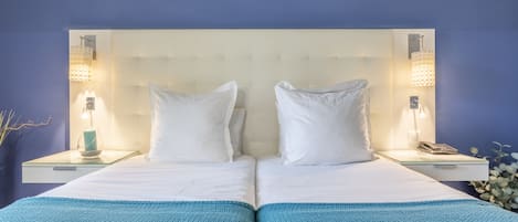Ein Doppelbett mit weißen Laken, zwei Nachttische mit Lampen und eine blaue Decke.