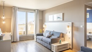 Een moderne woonkamer met een grijze bank, een witte bijzettafel en een groot raam met gordijnen.
